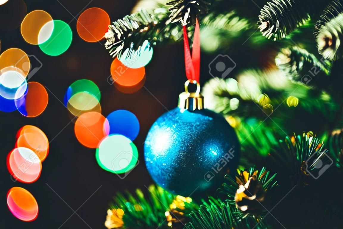 Blue Christmas ball on the spruce Christmas tree with multicolored bokeh round garland lights background