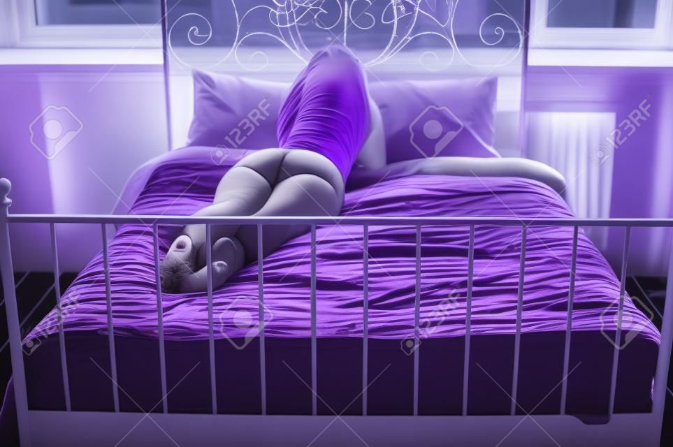 mollig vrouwtje in lingerie liggend op zijn buik op het paarse bed en kijkend uit het raam
