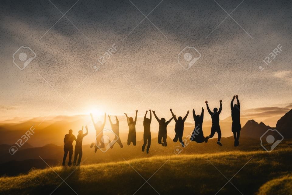 Grupo de personas con las manos en alto saltando sobre la hierba en las montañas al atardecer