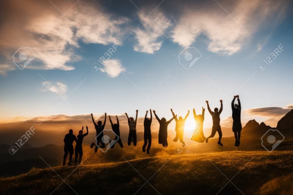 Groupe de personnes avec les mains en sautant sur l'herbe dans les montagnes au coucher du soleil