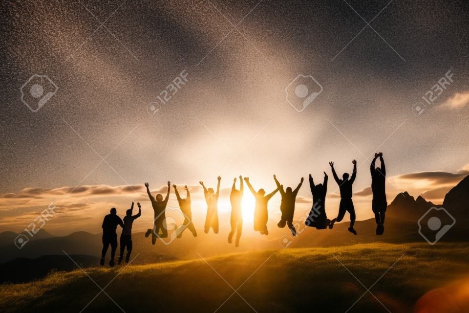 Groupe de personnes avec les mains en sautant sur l'herbe dans les montagnes au coucher du soleil