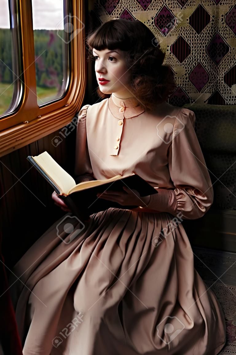 Junge Frau in beige Weinlesekleid des frühen 20. Jahrhunderts Lesebuch im Coupé von Retro-Eisenbahn