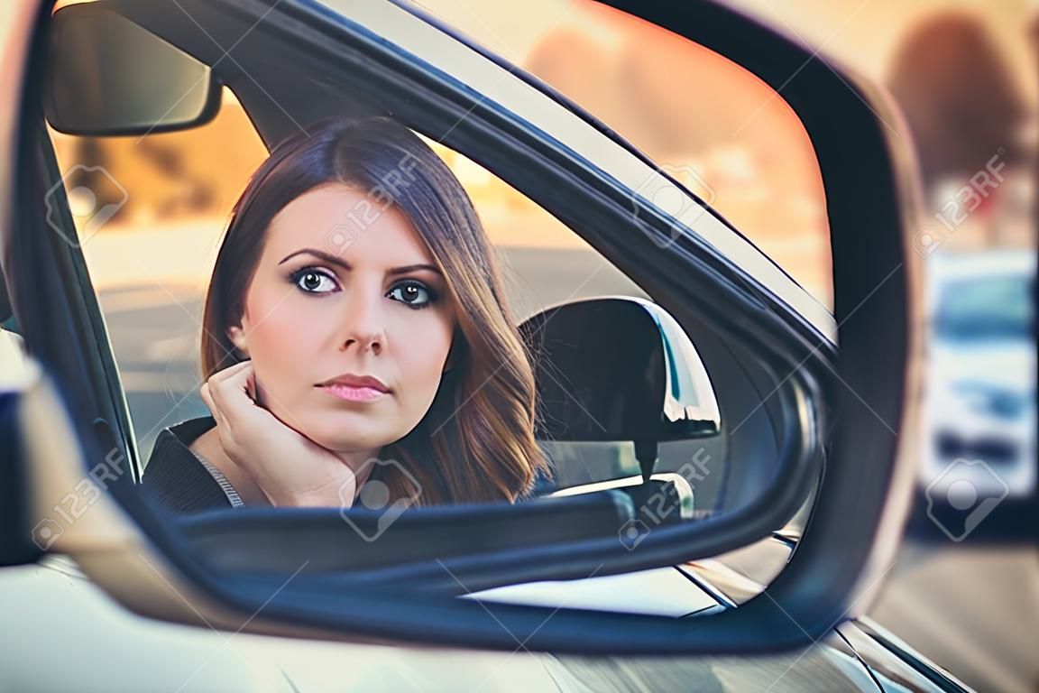 Rear view of attractive young woman in casual wear looking in rear-view mirror in her car