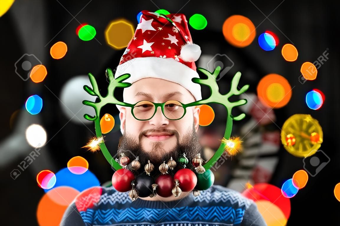 Un homme portant un chapeau de père noël et des jouets décoratifs sur sa barbe accueille la bonne année dans un cercle de lumières bokeh colorées. Photo de haute qualité