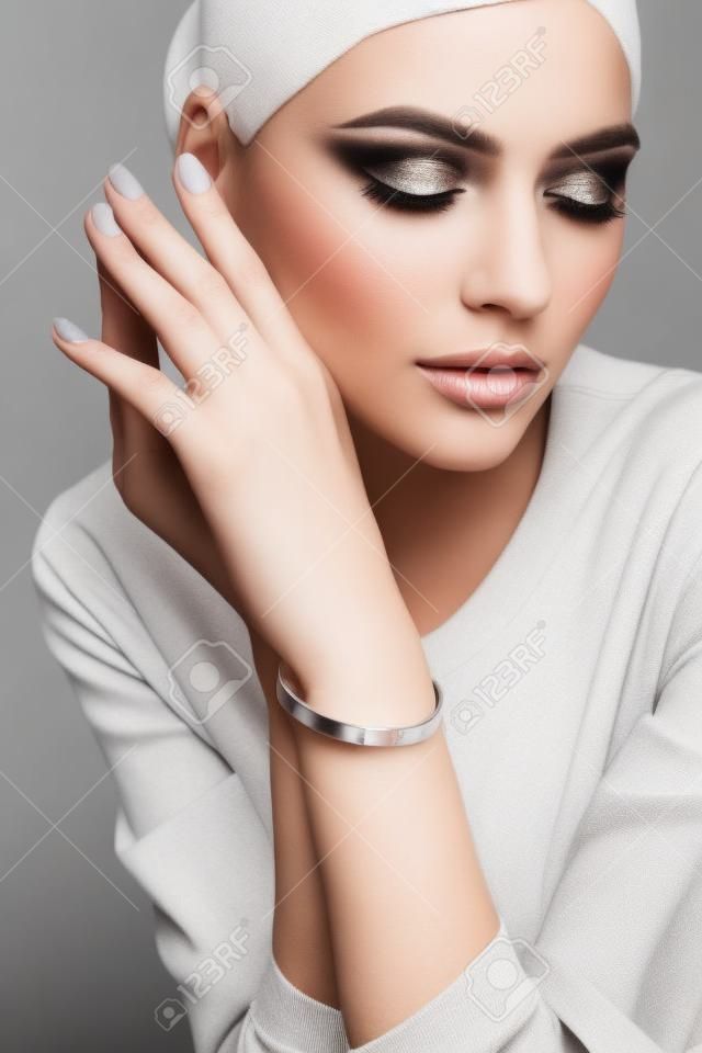 Cosecha de modelo femenino joven con maquillaje perfecto que presenta pulsera de plata minimalista. Retrato de mujer posando en estudio, aislado sobre fondo gris. Concepto de joyería.