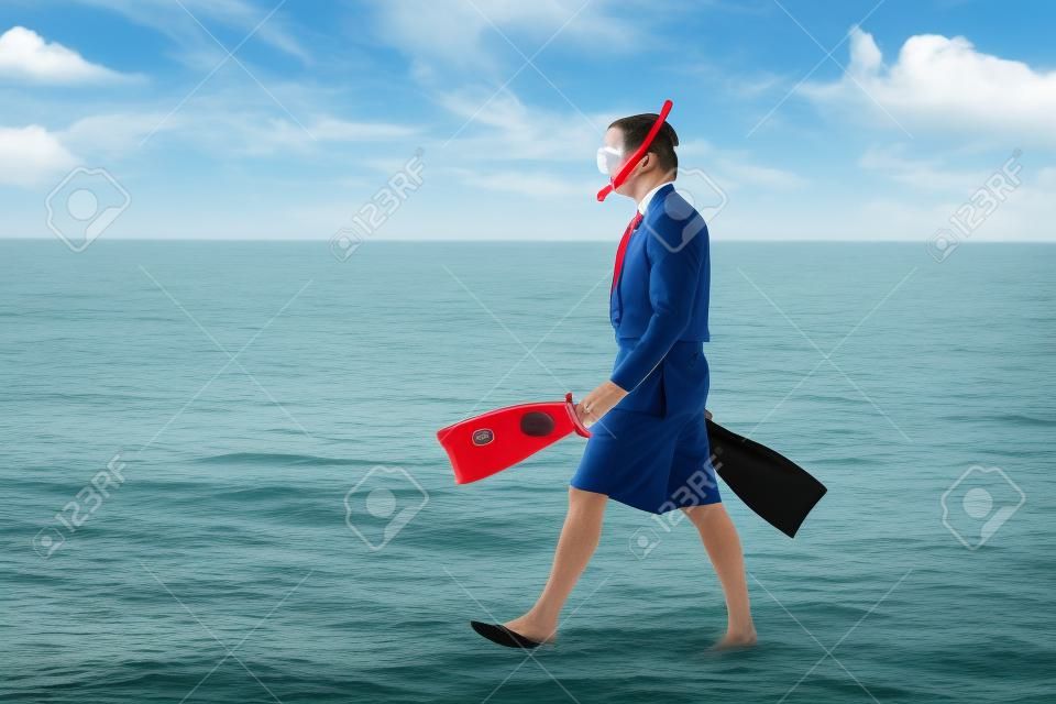 Businessman entering the ocean waters wearing snoring mask with flippers and wearing formal clothes with red tie entering water on the beach