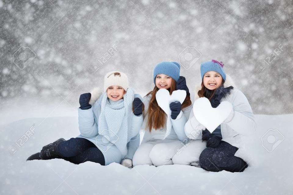 Three happy girls with heart made of snow, standing together outside in winter