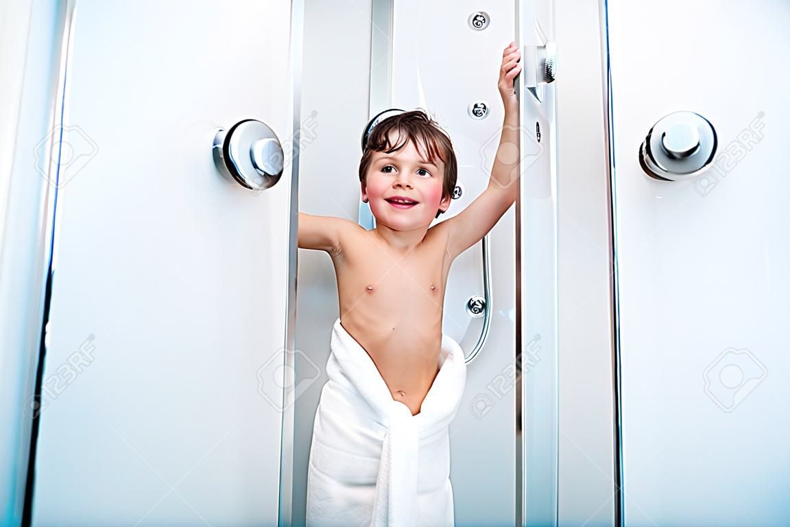 Petit garçon enfant couverte en blanc blanchi sortir de la cabine de douche tenant portes et souriant