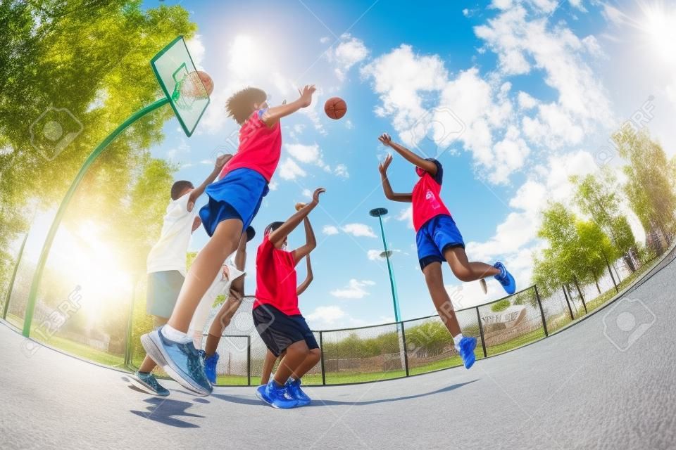 Fisheye view of teenagers playing basketball game together on the playground during sunny summer day