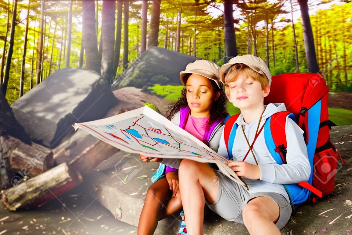 Two kids in forest navigate with map treasure hunt