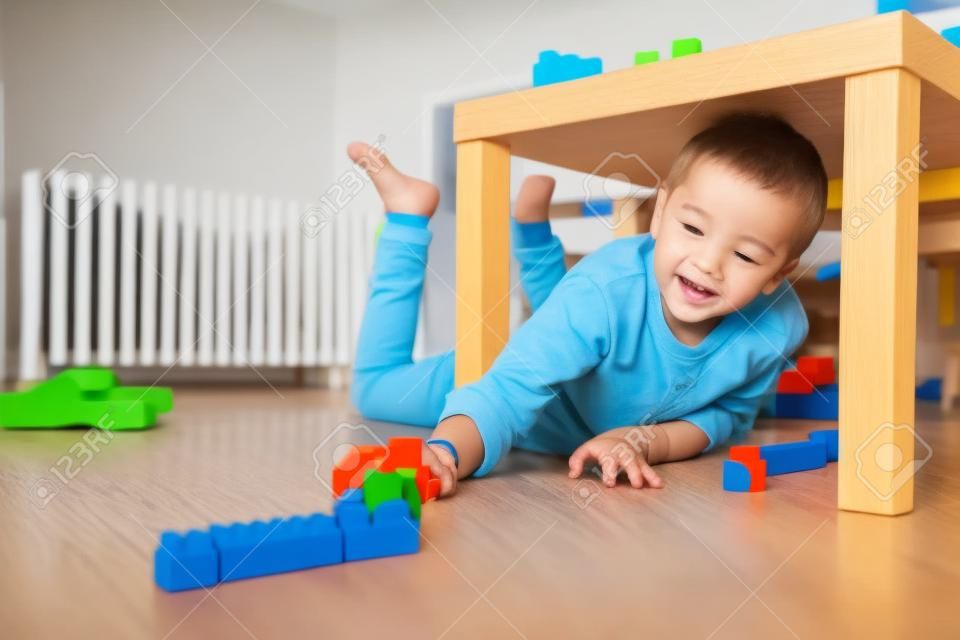Chłopiec bawi się klockami pod stołem w pokoju dziecięcym leżącym na podłodze