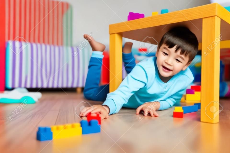 Chłopiec bawi się klockami pod stołem w pokoju dziecięcym leżącym na podłodze