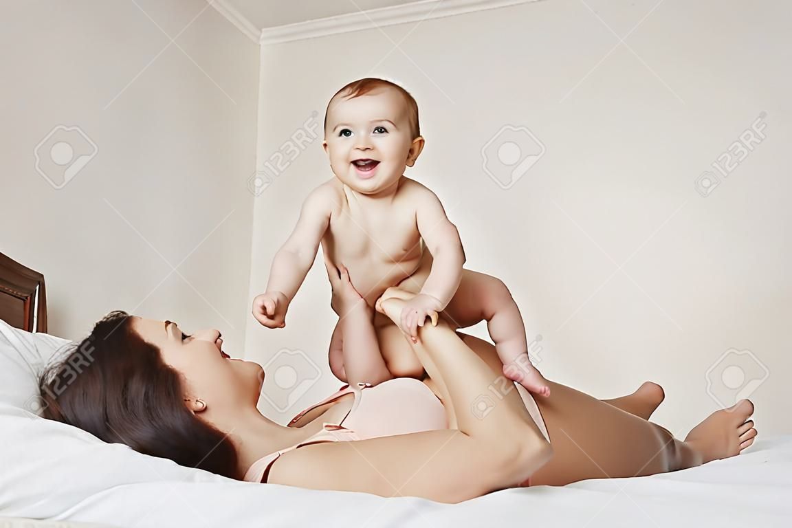 쾌활한 아름 다운 엄마와 집에서 침대에 누워 기쁨 미소를 재생하는 그녀의 아기.