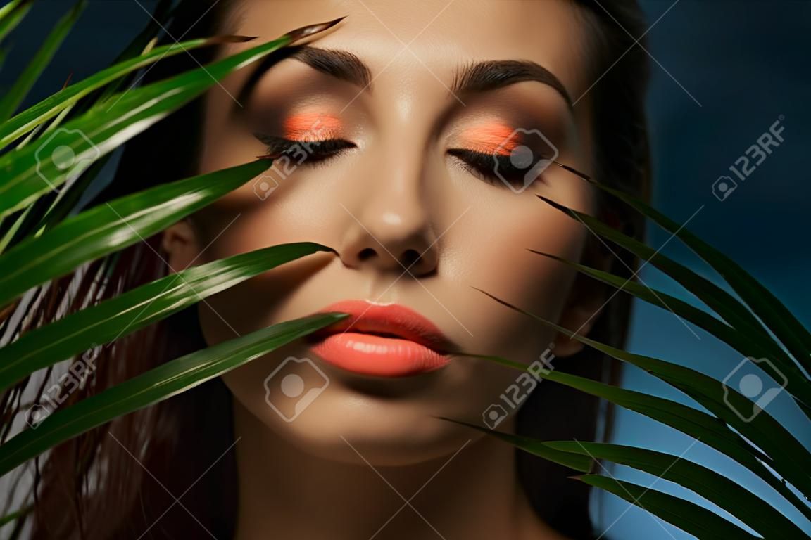 Beautiful woman face under exotic green leaves. Fashion photography.