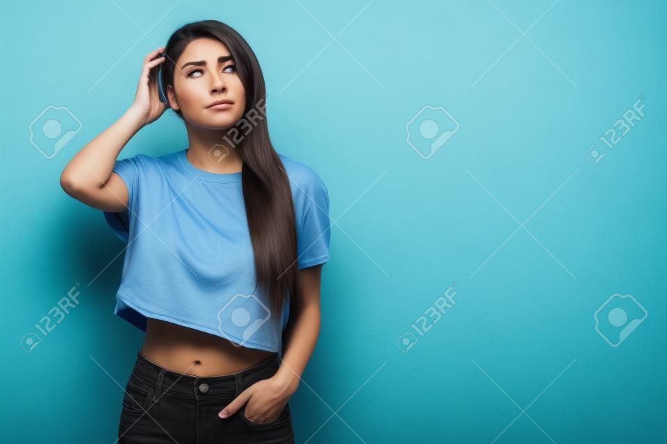 Portrait of confused gloomy and perplexed cute female coworker in cropped blue t-shirt scratching head clueless and troubled frowning having uneasy times struggling to find answer over grey wall