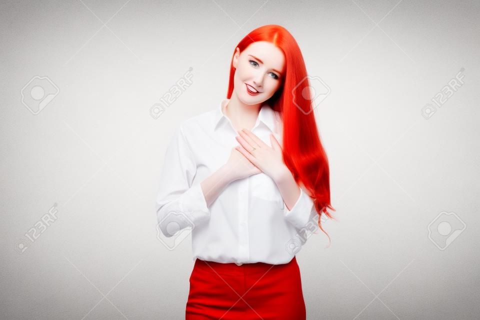 Manager di giovane donna con i capelli rossi e la pelle pallida, tenendo le mani sul cuore e ringraziandoti, essendo grato, esprimendo gratitudine in piedi su sfondo bianco