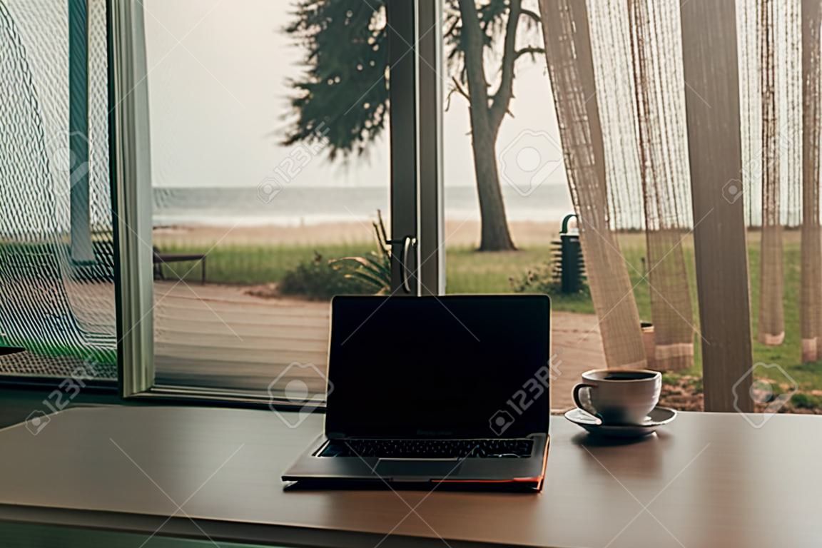 Concept van het werk en ontspannen. Laptop en hete koffiebeker bij de deur stap met herfst uitzicht op het strand.