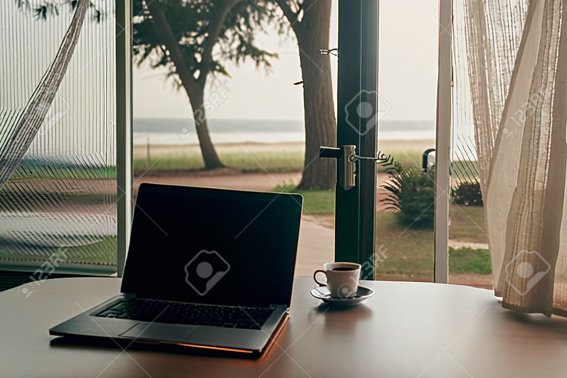 Concept van het werk en ontspannen. Laptop en hete koffiebeker bij de deur stap met herfst uitzicht op het strand.