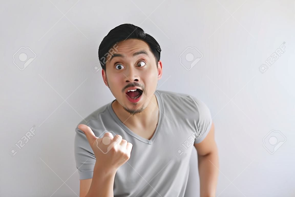 Wow e rosto surpreso do homem asiático em t-shirt cinza com ponto de mão no espaço vazio.