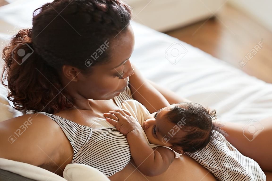High angle portrait of young African-American mother breastfeeding cute baby boy with child looking at camera, copy space