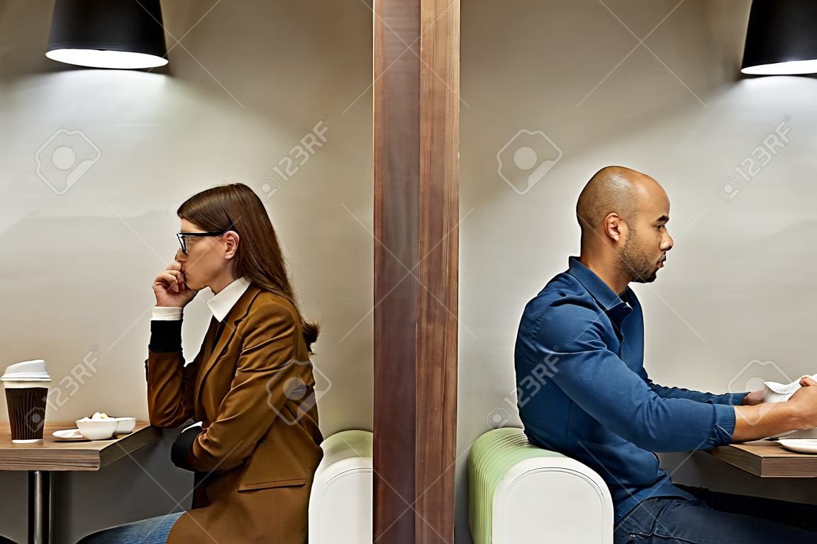 Minimal side view portrait of two adult people separated by wall while sitting in separate cafe booths, copy space