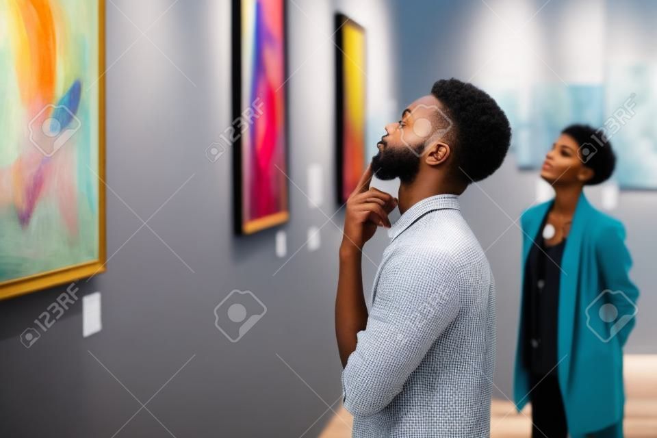 現代アートギャラリーの展示会、コピースペースを探索しながら絵画を見ている若いアフリカ系アメリカ人男性の側面図の肖像画