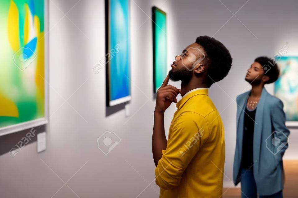 現代アートギャラリーの展示会、コピースペースを探索しながら絵画を見ている若いアフリカ系アメリカ人男性の側面図の肖像画