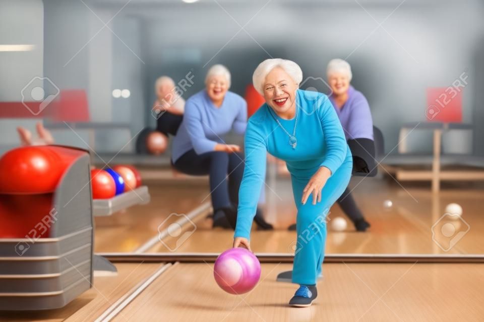 Pełnometrażowy portret radosnej starszej kobiety grającej w kręgle z grupą przyjaciół w tle, kopia przestrzeń