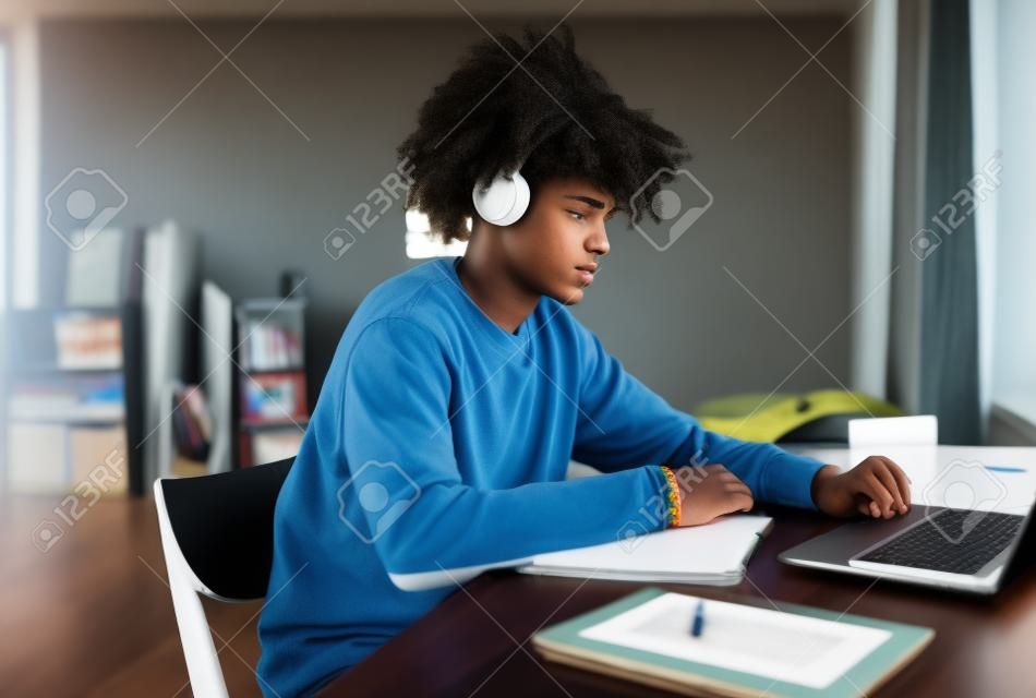 Widok z boku portret afroamerykańskiego nastolatka studiującego w domu lub w akademiku i korzystającego z laptopa, miejsce na kopię