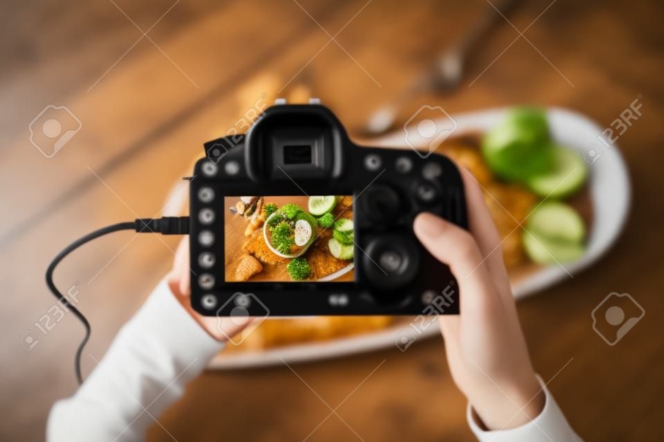 Vista superior de primer plano de un fotógrafo de alimentos que sostiene una cámara digital con una imagen en la pantalla mientras trabaja en un estudio en casa, copia espacio