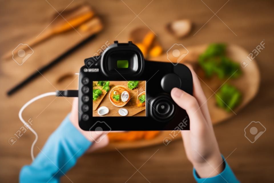 홈 스튜디오에서 작업하는 동안 화면에 이미지가 있는 디지털 카메라를 들고 있는 음식 사진 작가의 상위 뷰, 복사 공간
