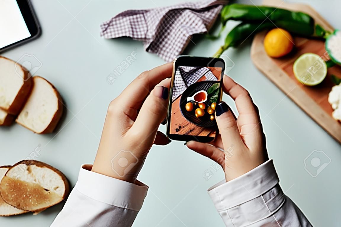 Vista superior de una mujer joven que toma una foto estética de la comida usando un teléfono inteligente en un estudio en casa, espacio para copiar