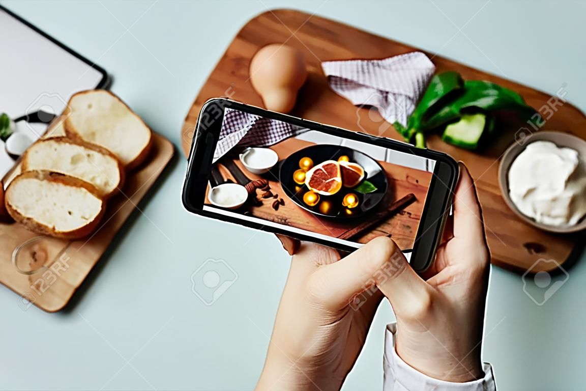Vista superior da mulher jovem que toma a foto estética da comida usando o smartphone no estúdio home, espaço da cópia