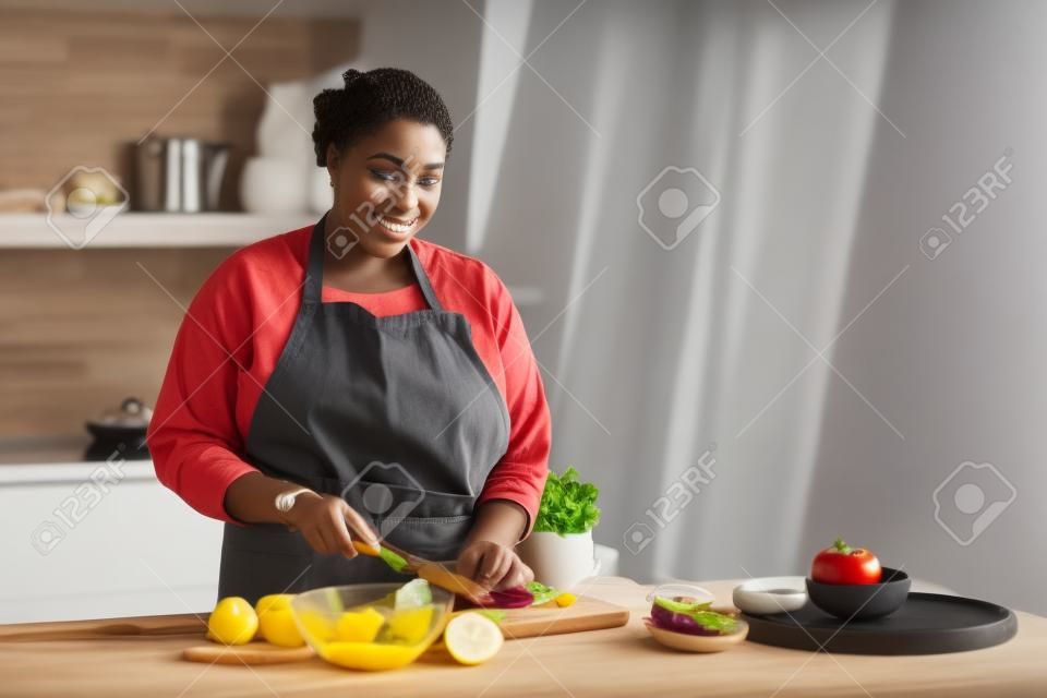 Talia w górę portret młodej czarnej kobiety gotującej zdrową sałatkę w kuchni i patrzącej na kamerę, kopia przestrzeń