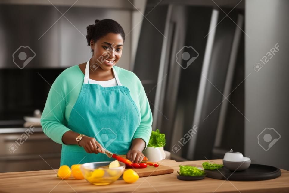 Talia w górę portret młodej czarnej kobiety gotującej zdrową sałatkę w kuchni i patrzącej na kamerę, kopia przestrzeń