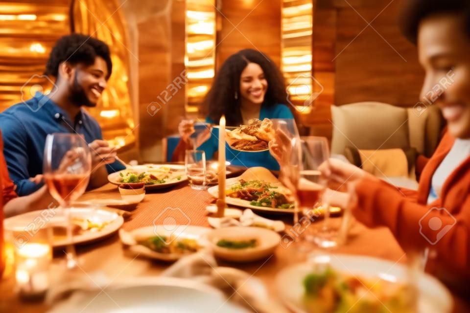 Retrato en tonos cálidos de diversos jóvenes disfrutando de una cena en la mesa en un ambiente acogedor