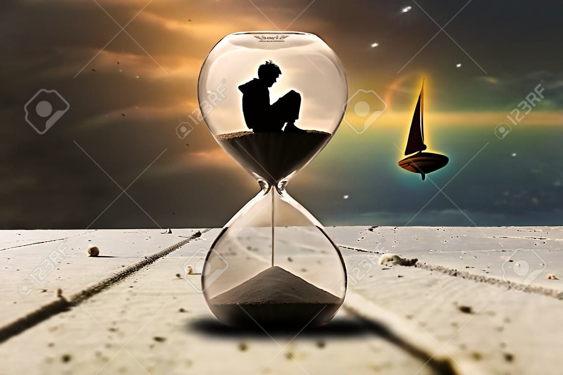 Alone man sitting in hourglass, boy looking up to the sky in the dark. Time traveling with sand watch on ocean. Sailing boat background