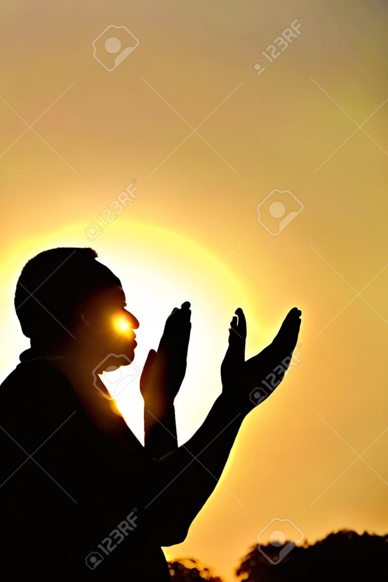 Silhueta de um muçulmano orando sobre o pôr do sol dourado