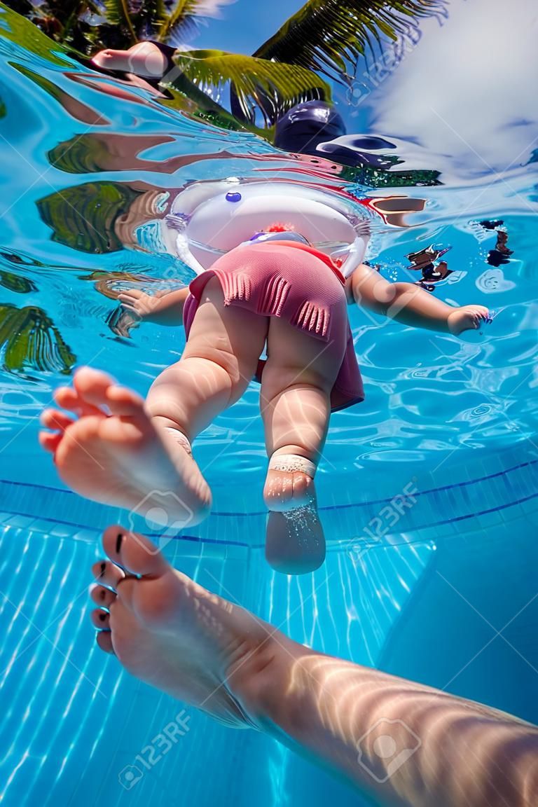 Father holding his little daughter feet while she swims in pool