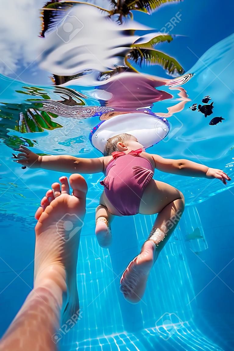Father holding his little daughter feet while she swims in pool