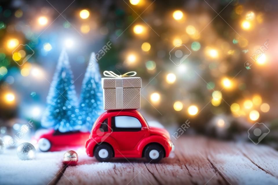 Decoração de ano novo e fundo para saudações com espaço livre para texto. Carro de brinquedo carrega um presente no fundo de árvores de Natal e luzes bokeh em uma madeira. 2020