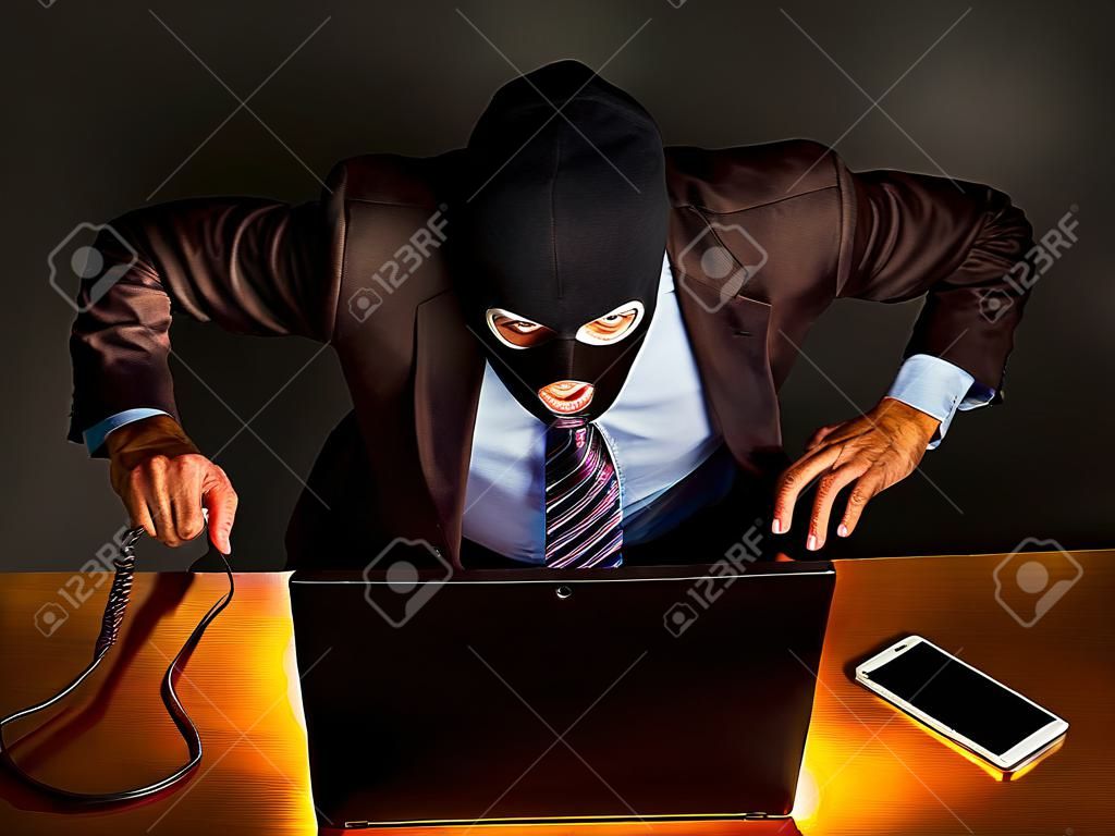 homme d'affaires représentatif en costume-cravate, mais portant un masque avec une cagoule couvrant son visage, se livre à un vol via Internet à partir d'un ordinateur portable