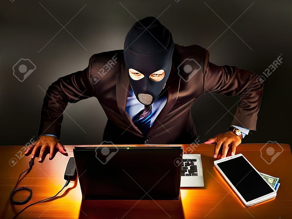 homme d'affaires représentatif en costume-cravate, mais portant un masque avec une cagoule couvrant son visage, se livre à un vol via Internet à partir d'un ordinateur portable