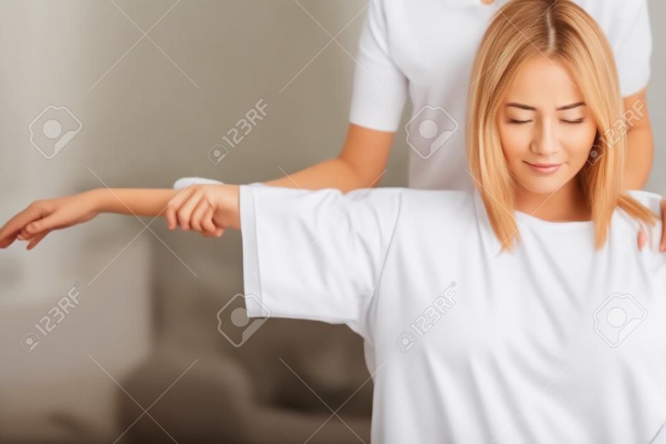 Женщина сидит в постели и получает массаж плеч и шеи.