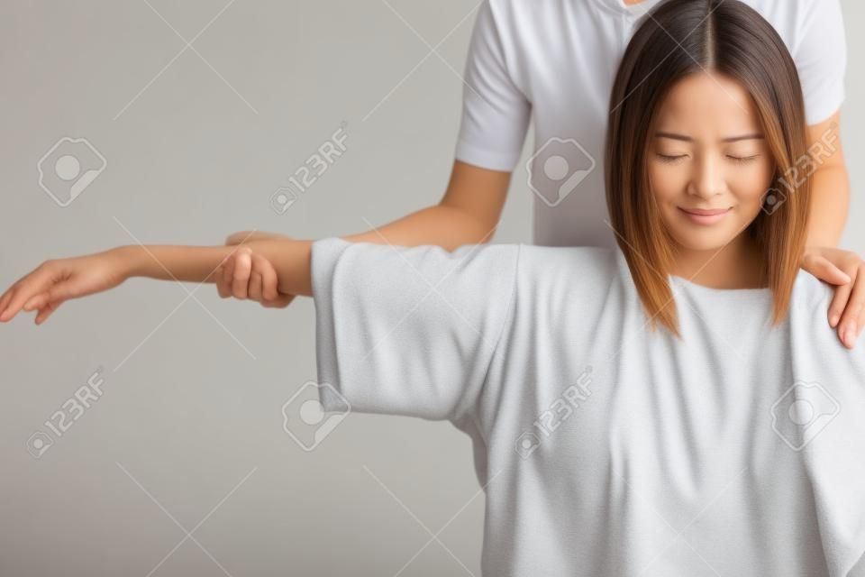 Женщина сидит в постели и получает массаж плеч и шеи.