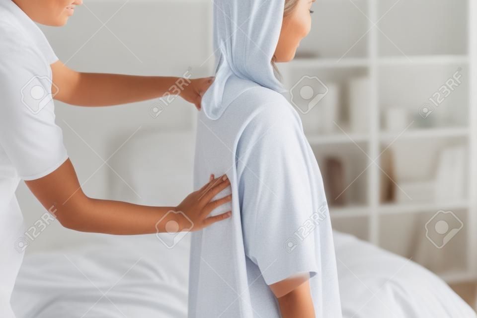 Kobieta siedzi w łóżku i odbiera masaż barku i szyi.