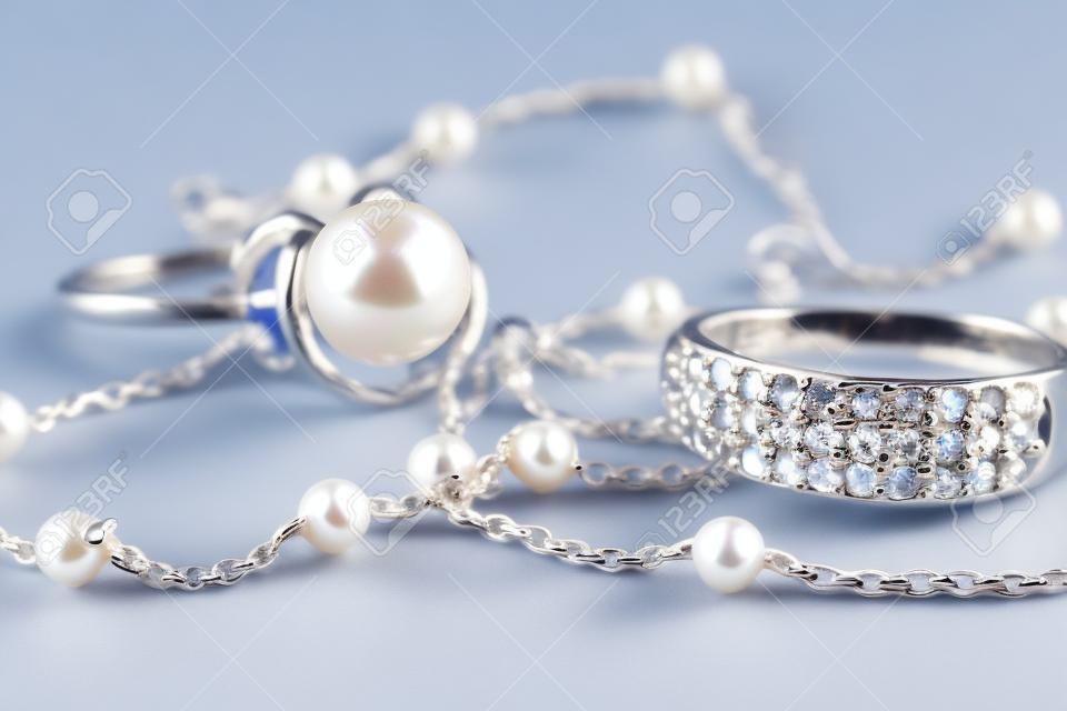 Silver ring with precious stones and pearl are together with a silver chain on acrylic