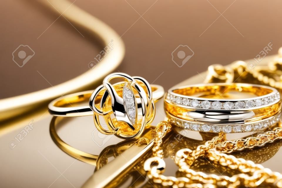 Gouden, zilveren ringen en kettingen van verschillende stijlen liggen samen op het reflecterende oppervlak