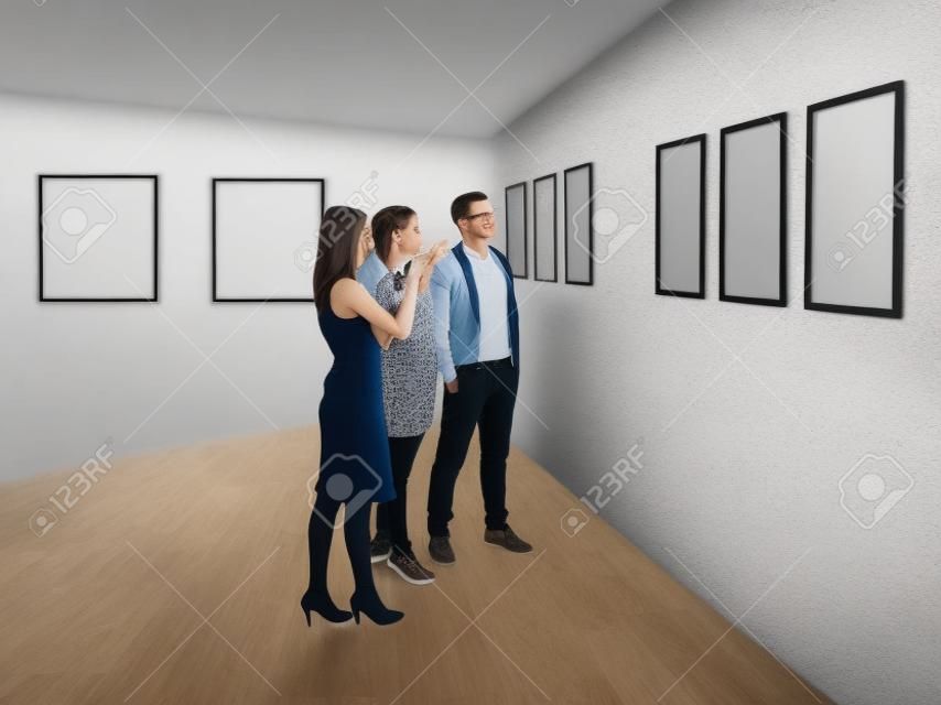 Gruppe von Menschen in einem Raum stading suchen und zeigte auf die leeren Rahmen auf weiße Wände angezeigt