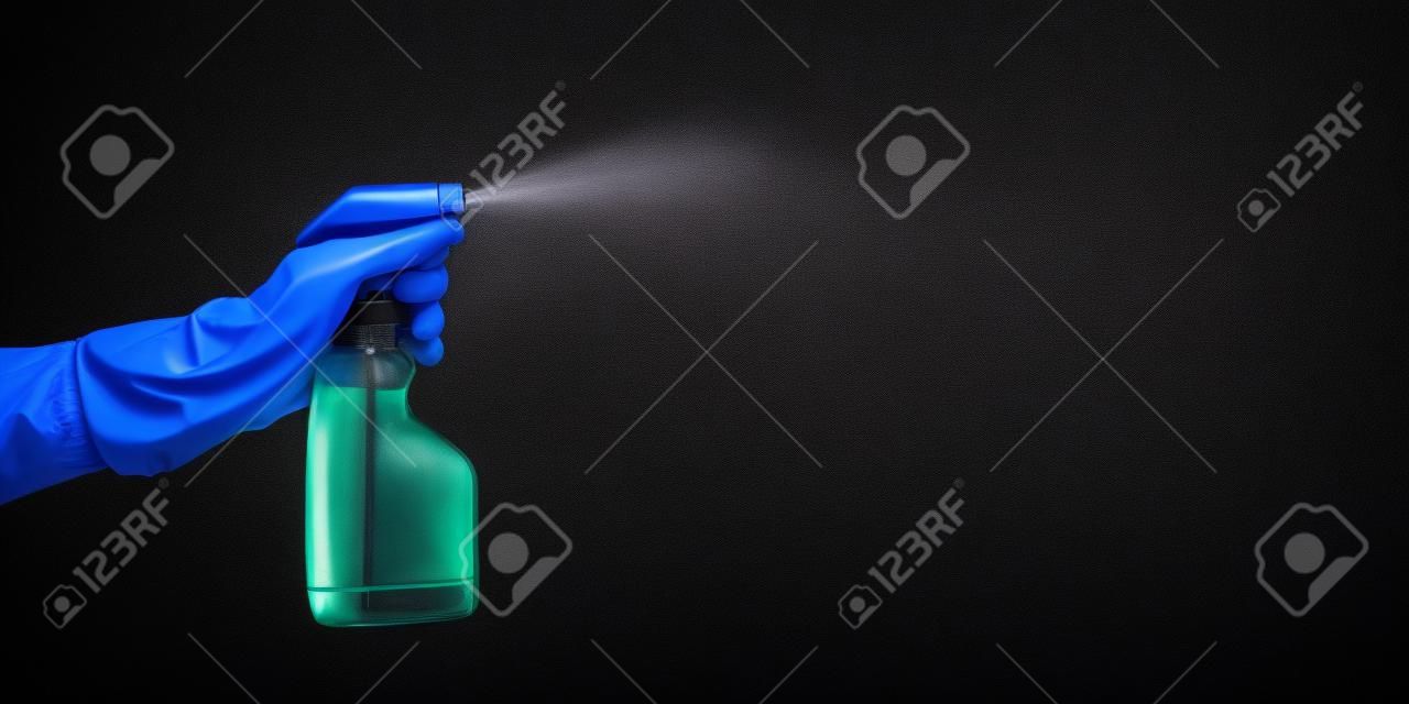 hand with rubber glove holding cleaning bottle and spraying liquid, on black background